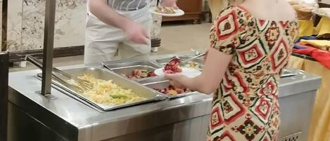 A buffet setup with multiple food trays and a person serving food.