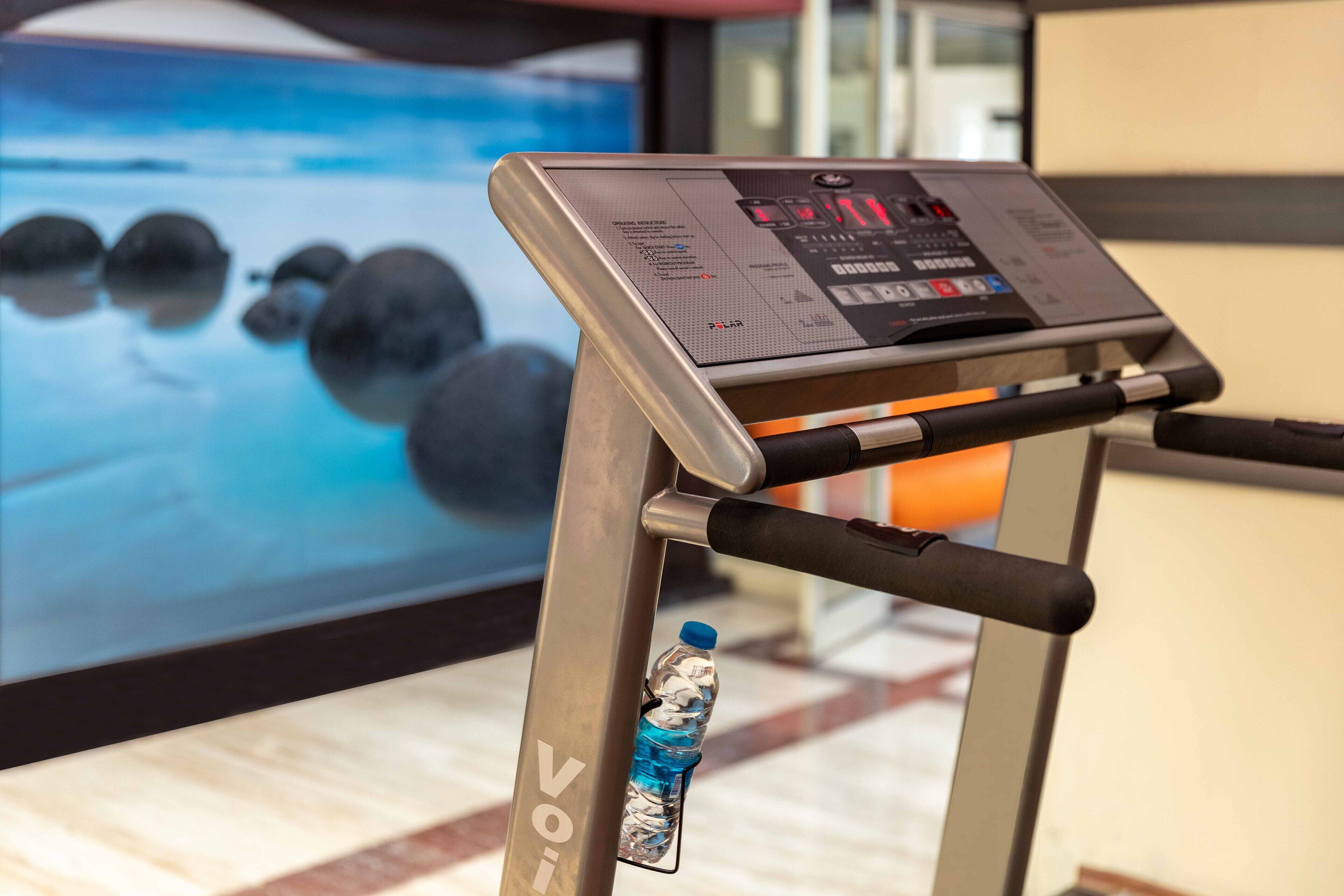 A treadmill with a digital display and a water bottle attached to its frame.