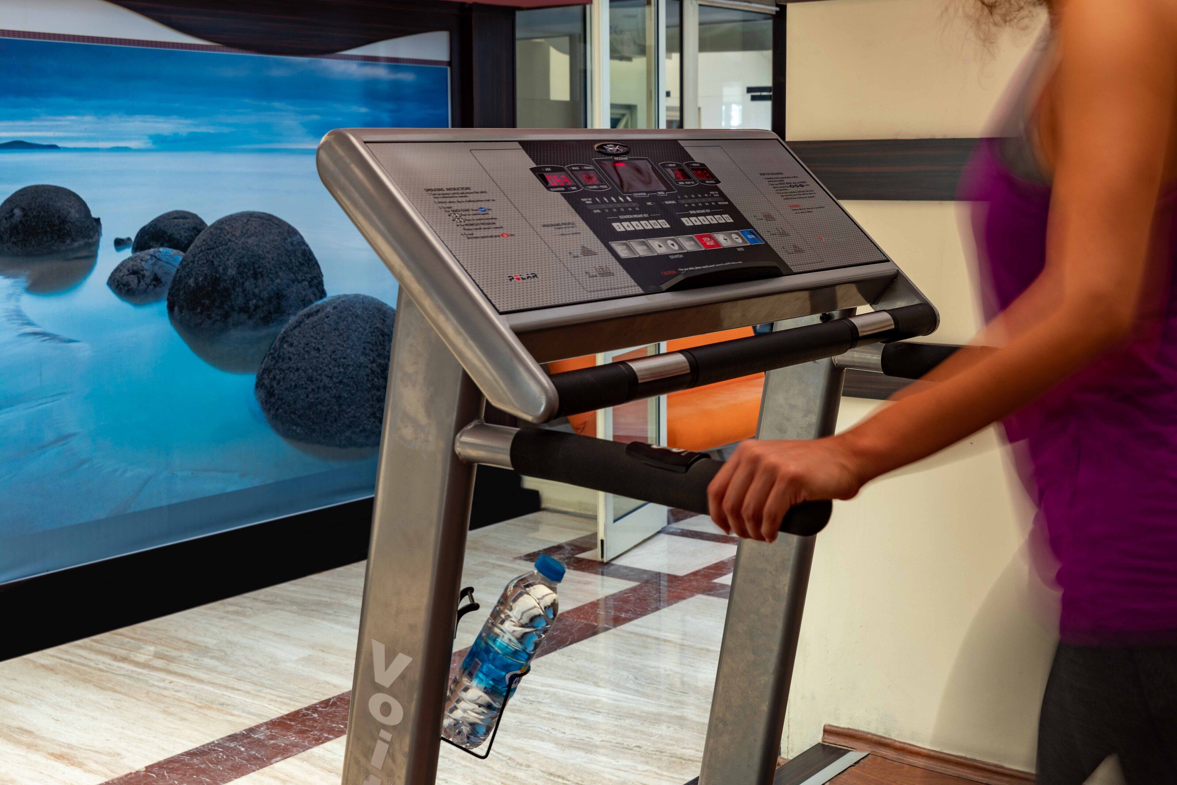 A treadmill with a digital display, a water bottle, and a large screen with a nature scene.