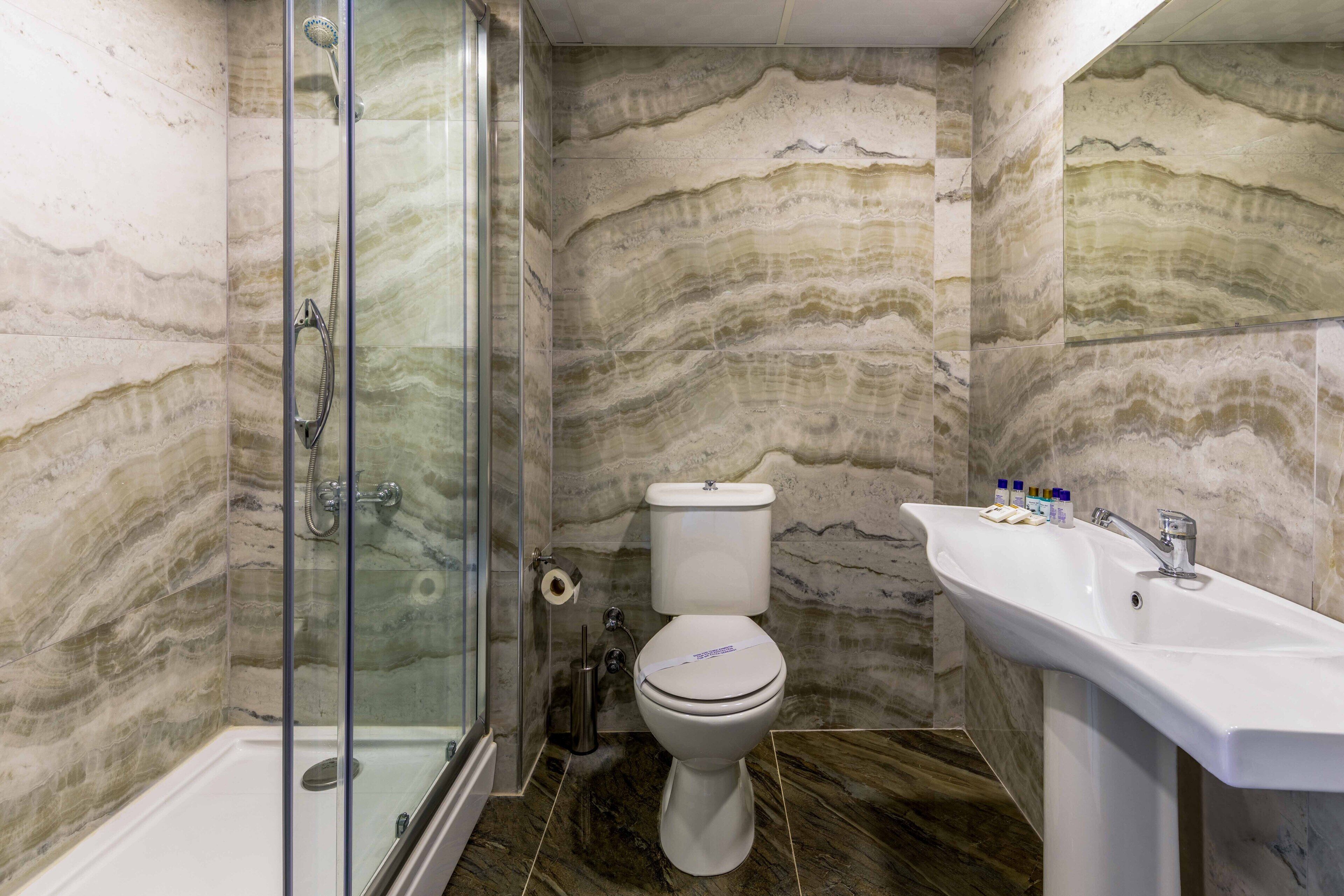 A bathroom with a shower, toilet, and sink, featuring marble walls and floors.