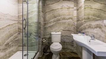 A bathroom with a shower, toilet, and sink, featuring marble walls and floors.