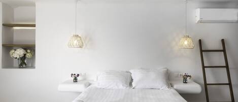 A minimalist hotel room with a large bed, white linens, two bedside tables with flower vases, and a wooden ladder.