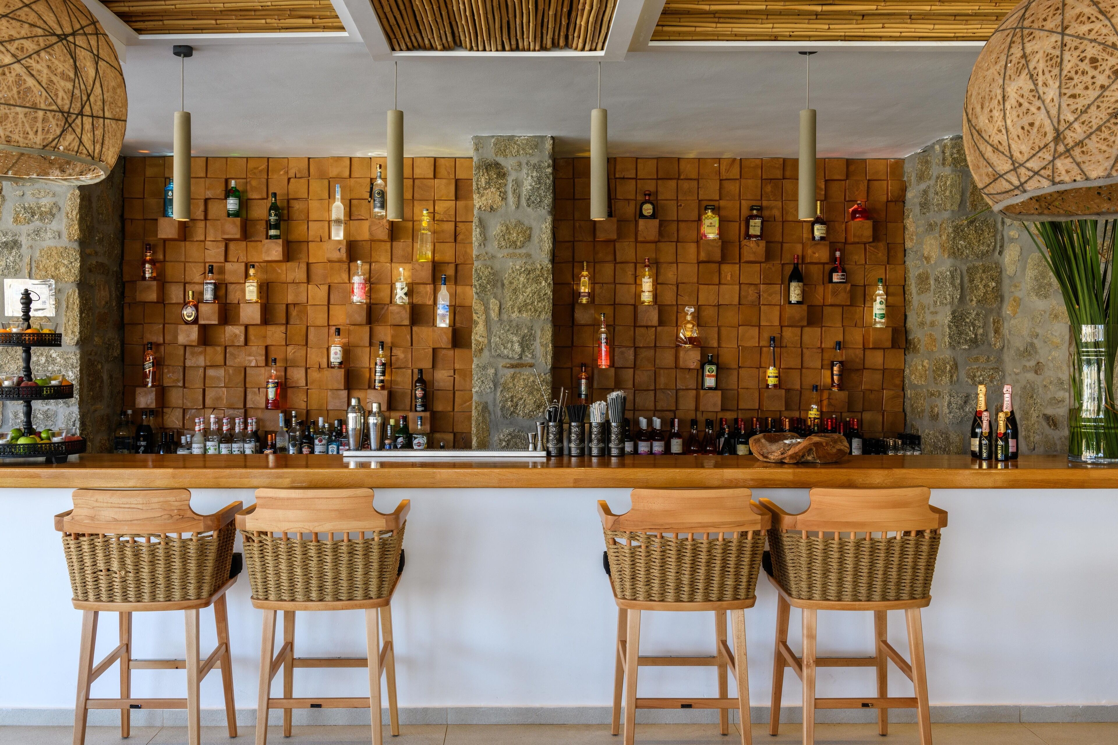 A bar area with a wooden counter, wicker barstools, and a wall of neatly arranged liquor bottles.