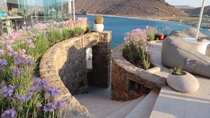 A stone pathway leading to a seating area with a view of the sea and a mountain. - Panormos Village Seaside Resort (Mykonos)