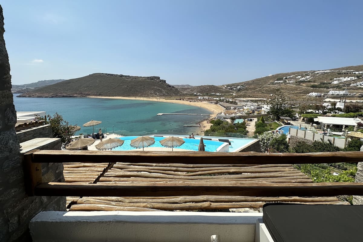 A coastal view with a swimming pool, beach, and hillside buildings.