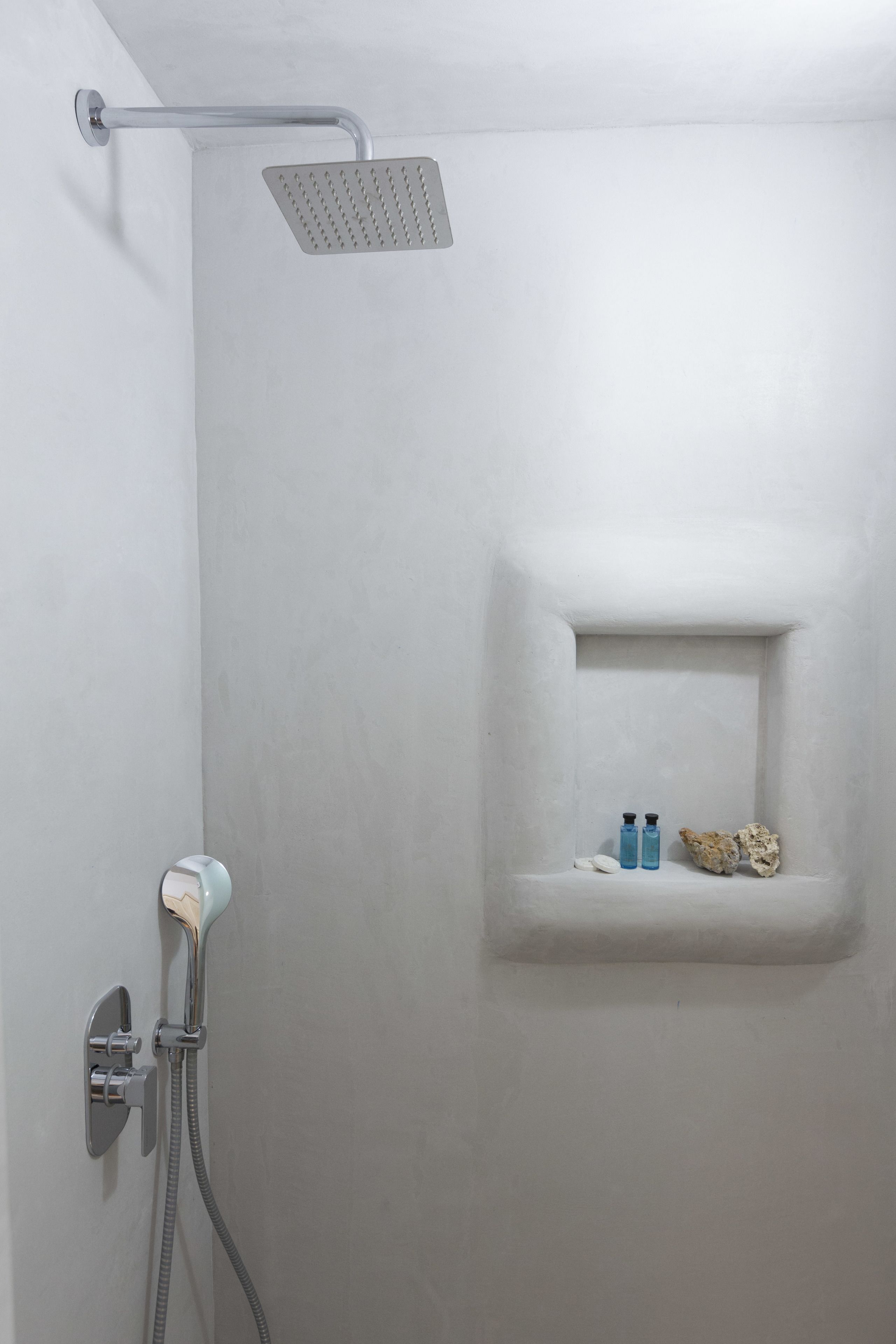 Een douche met een handdouche, een douchekop aan de muur, en een plank met toiletartikelen.