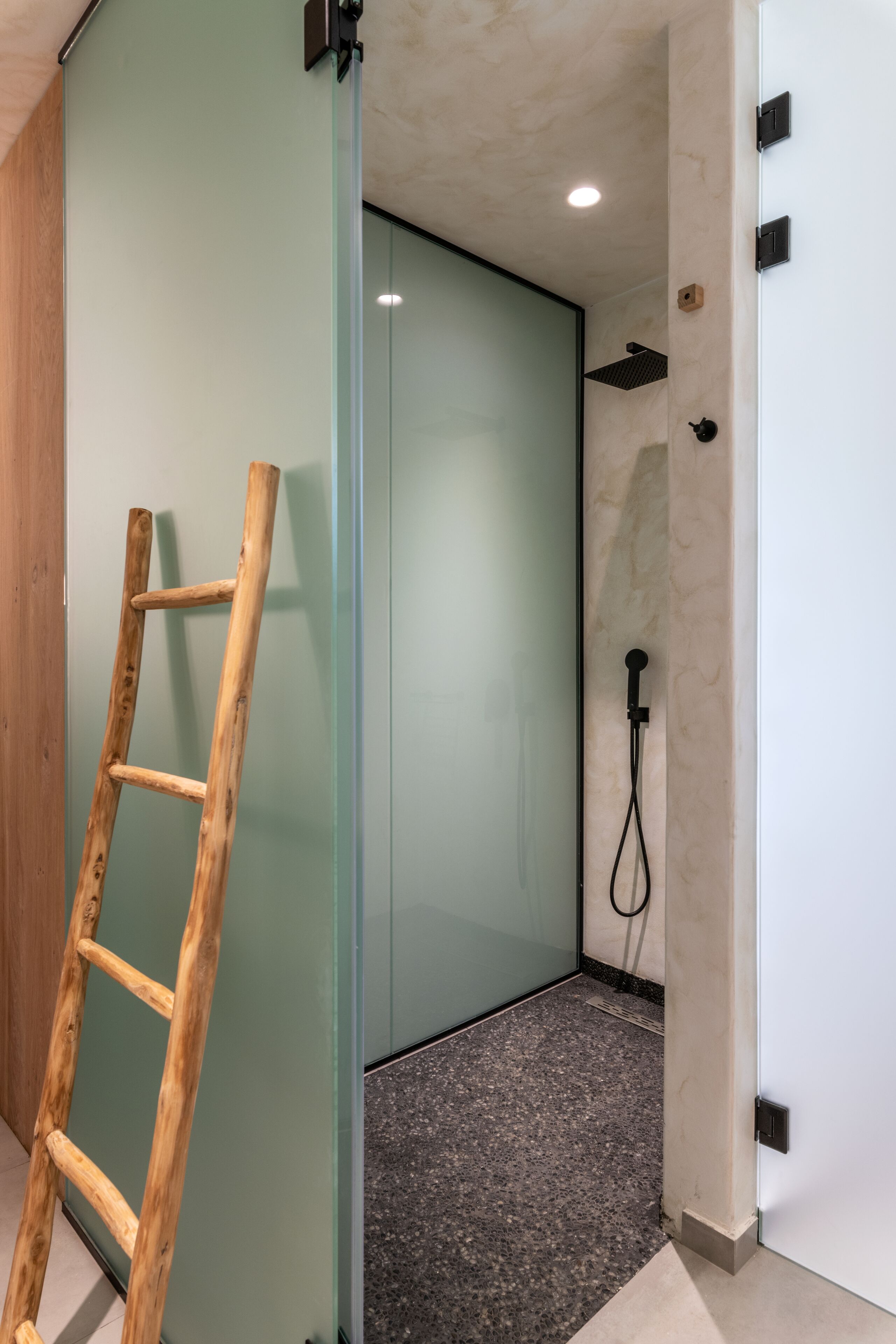 Un baño con ducha, una escalera de madera y un separador de vidrio.