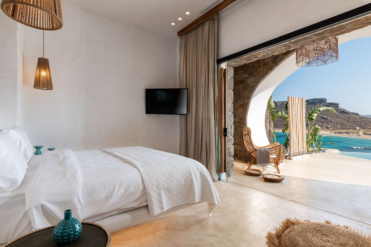 A bedroom with a bed, a TV, and a view of the beach.