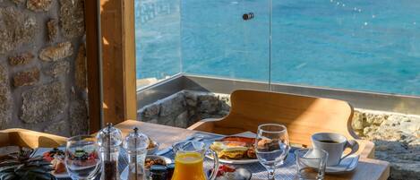 A breakfast table with various food items and drinks, overlooking a beach and ocean view.