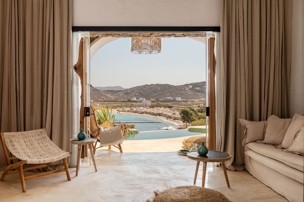 A room with a view of a beach and mountains, featuring a sofa, a chair, and a table with decorative items.
