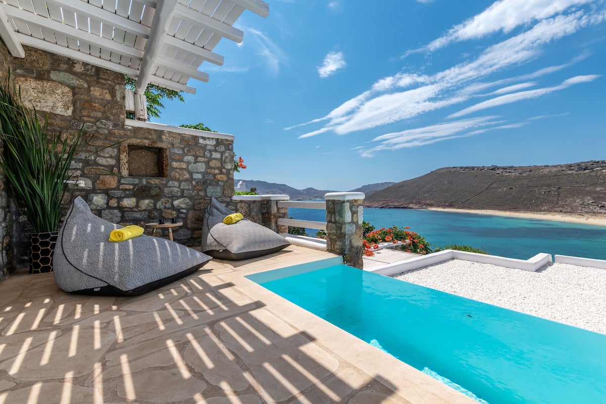 A pool area with stone walls, a pergola, and a view of the sea.