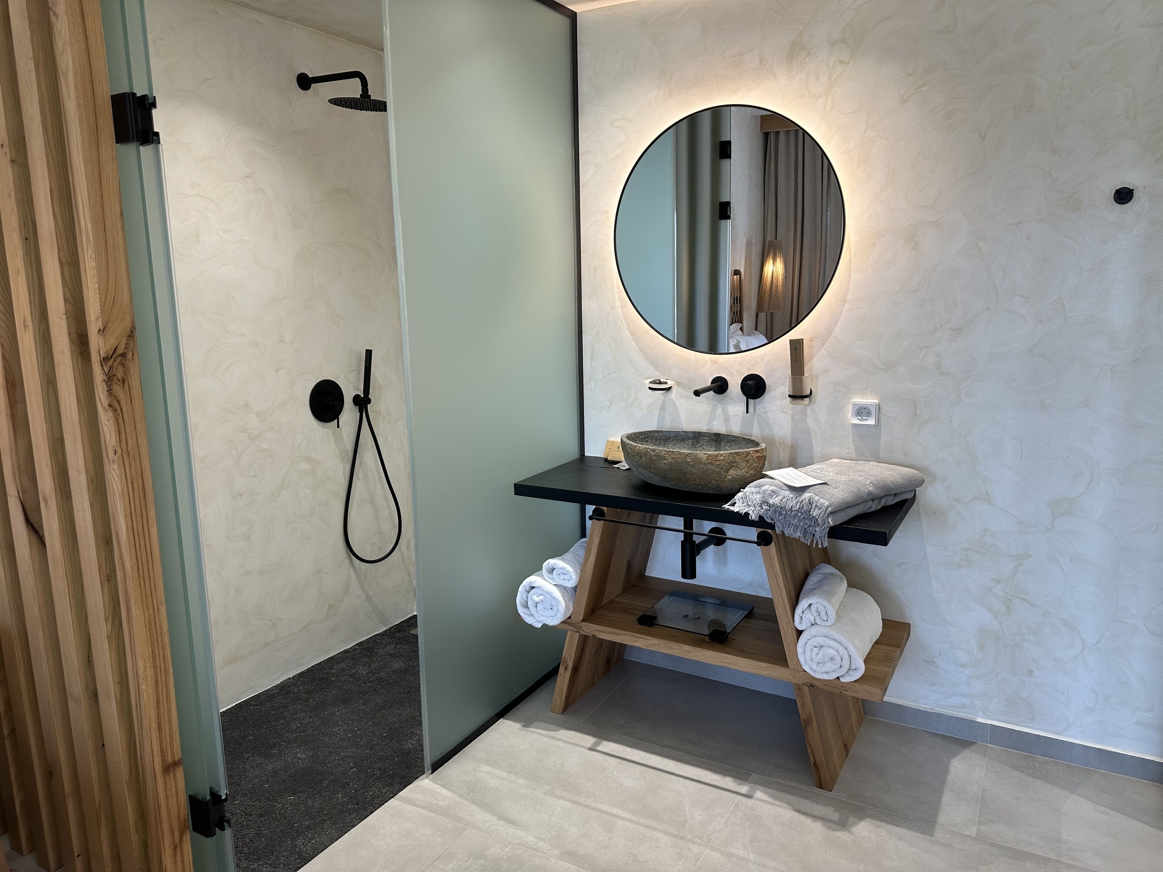 A bathroom with a wooden vanity, a round mirror, a stone basin, and a towel rack.