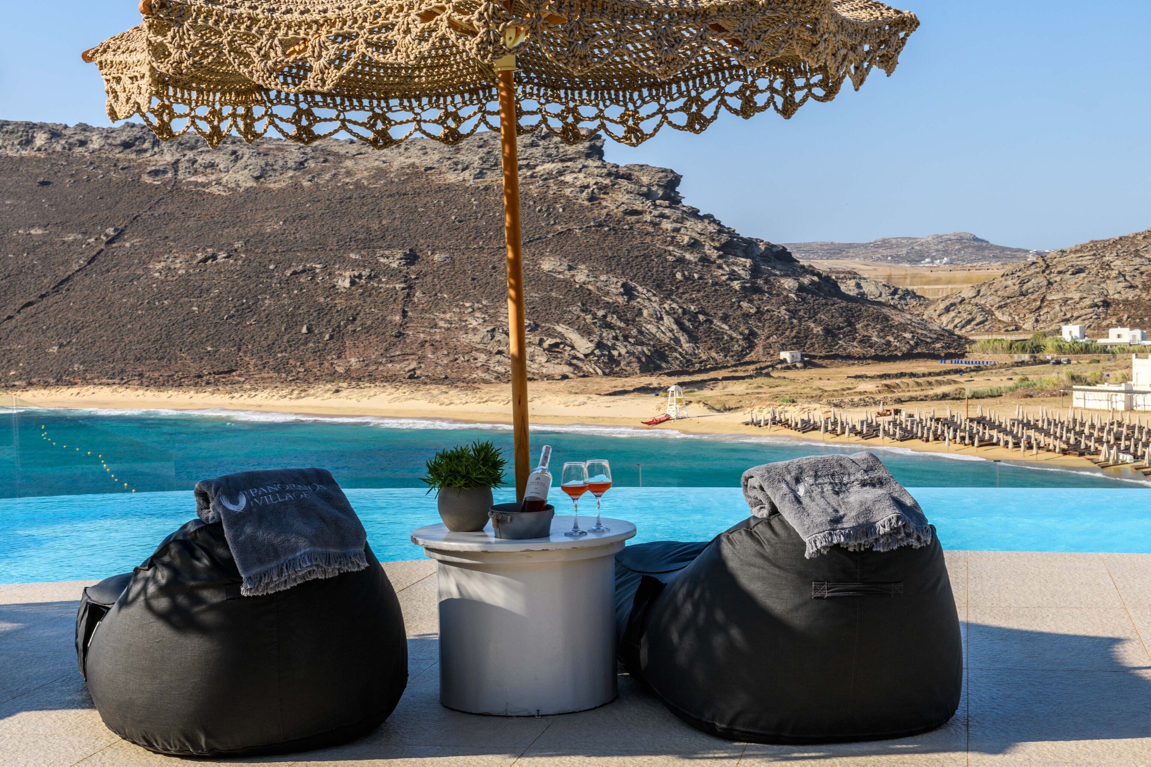 A poolside area with two bean bags, a table with a bottle and glasses, and a decorative umbrella.