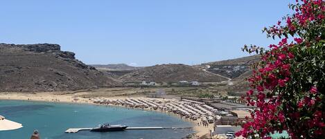 A seaside view with a beach, boats, and a row of umbrellas.