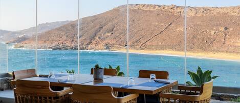 Una mesa para cuatro con sillas de mimbre, con vistas a una playa y montañas.