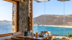 A dining table with chairs and a view of the ocean. - Panormos Village Seaside Resort (Mykonos)