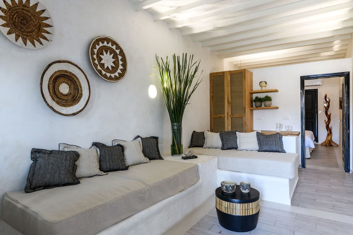 A modern living room with a sofa set, decorative wall art, a tall plant, and a wooden cabinet.