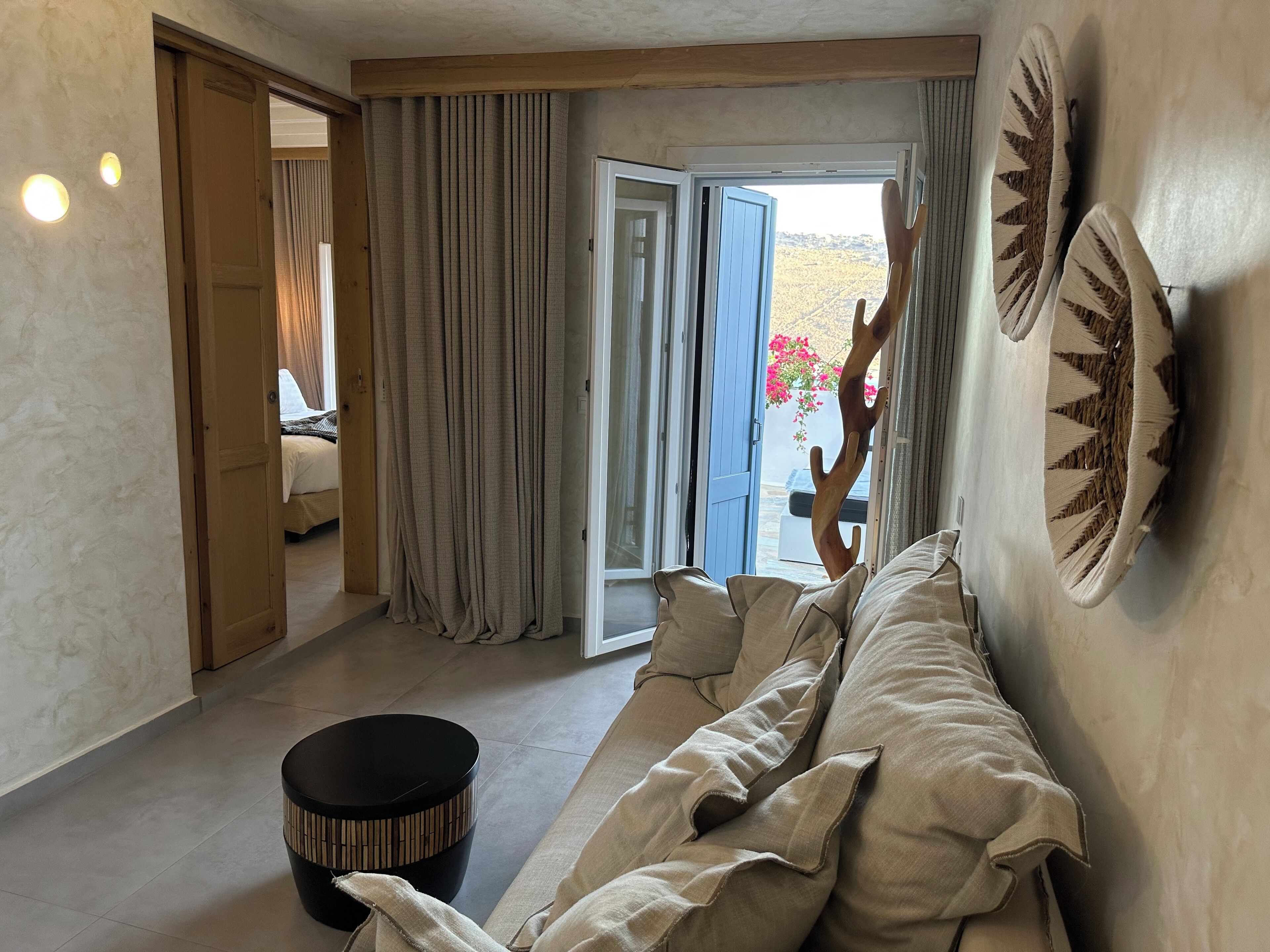 A living room with a sofa, a round black table, and a door leading to a balcony with curtains.