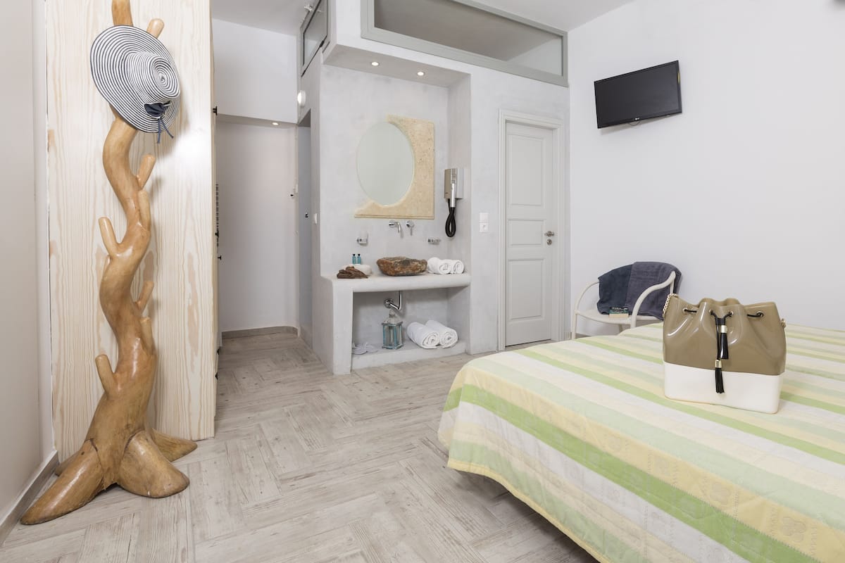 A hotel room with a wooden sculpture, a bed with a striped bedspread, a television on the wall, and a bathroom with a mirror and sink.