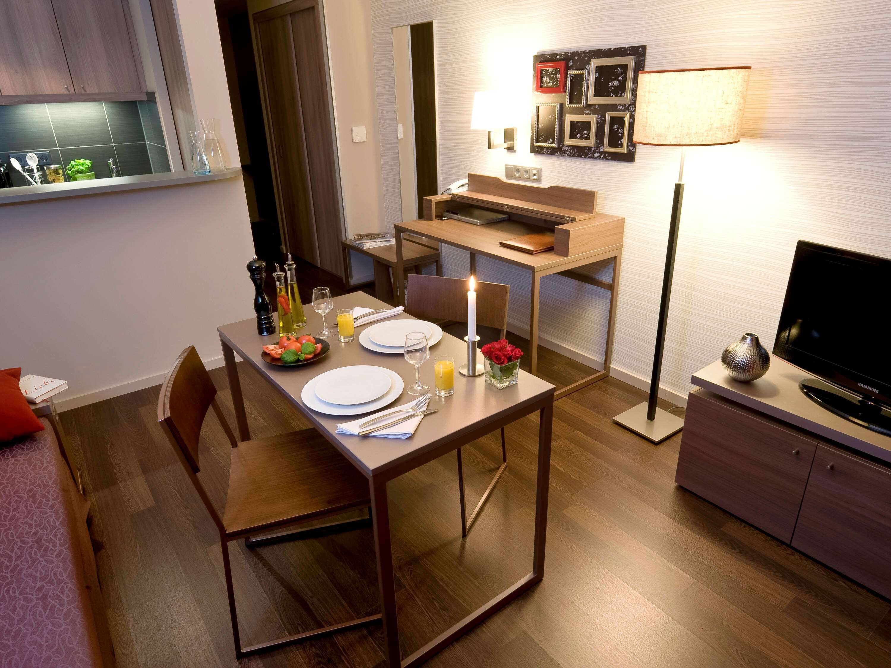 Un comedor moderno con una mesa de madera preparada para dos personas, un televisor y una lámpara.