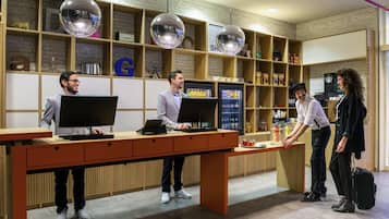 A reception desk with three employees, a coffee machine, and shelves with various items.