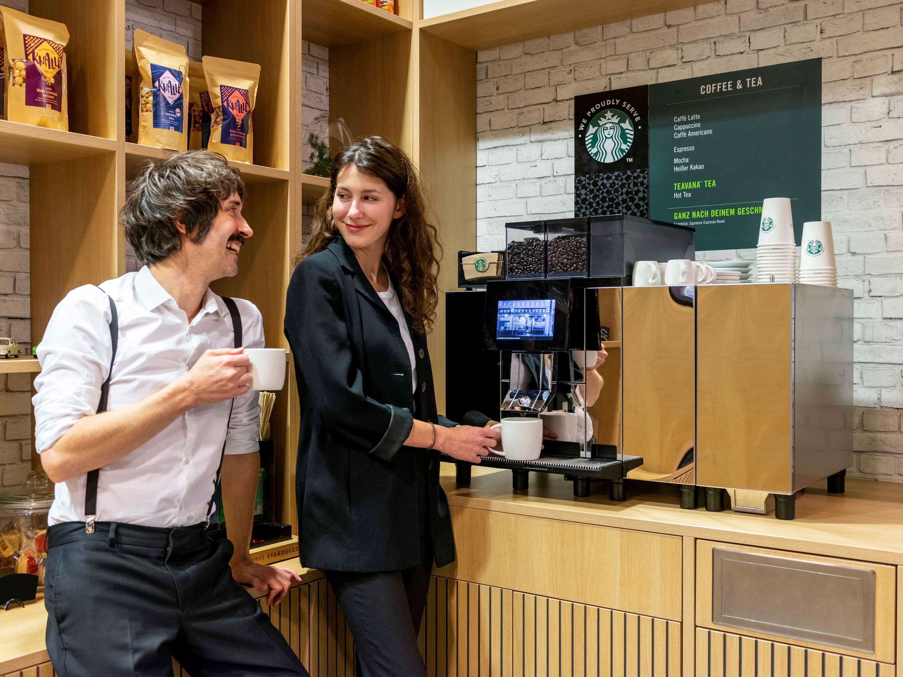 Mostrador de cafetería con un panel de menú que muestra opciones de café y té, una máquina de café y una exhibición de granos de café.