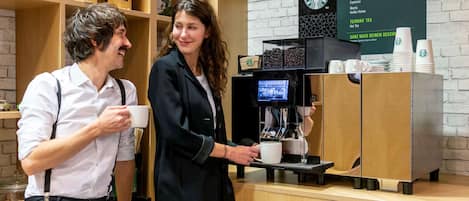 A coffee shop counter with a menu board displaying coffee and tea options, a coffee machine, and a display of coffee beans.