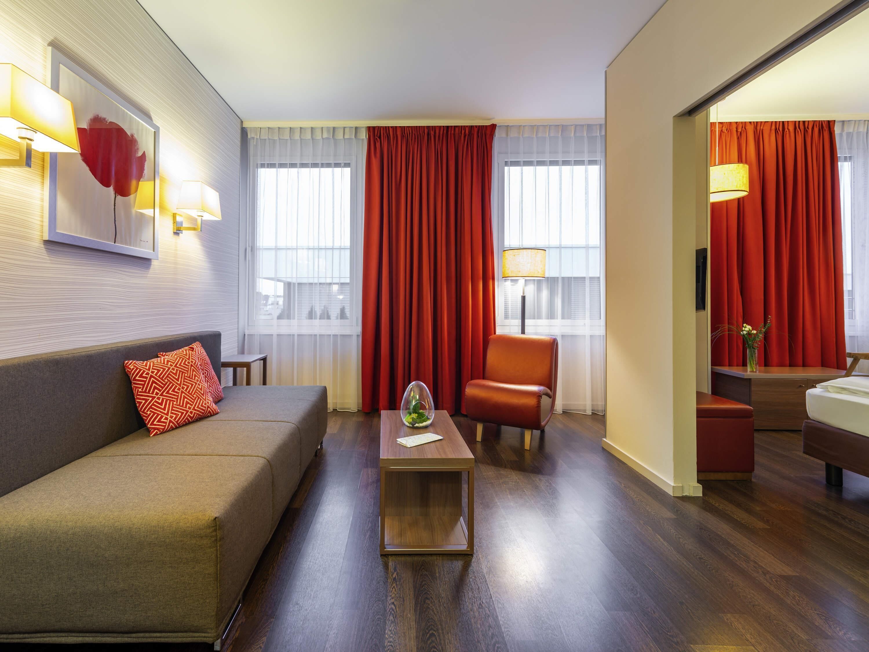 A hotel room with a sofa, armchair, and a small table with a vase.