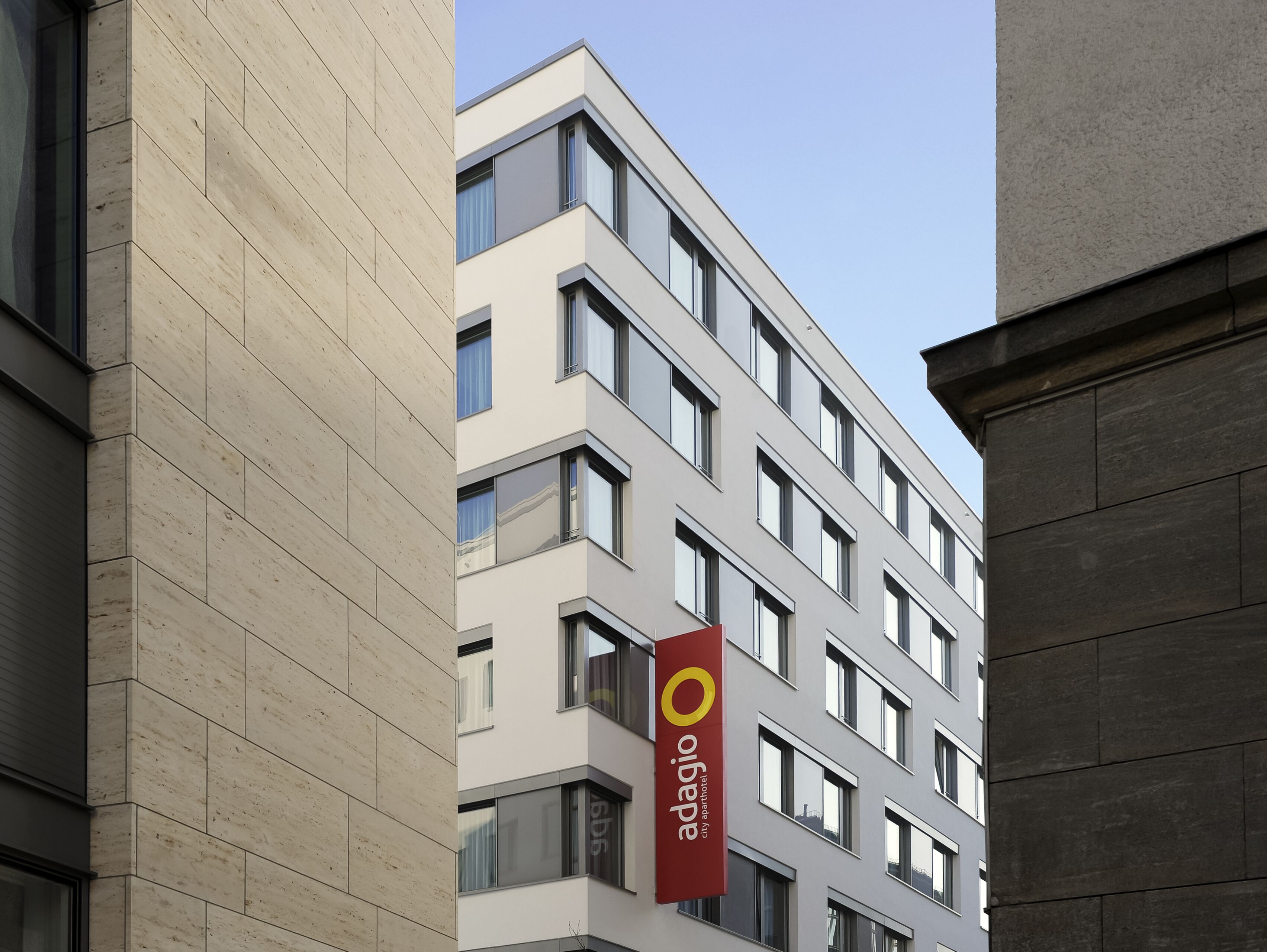 A modern building with a red banner displaying "adagio city apartment hotel".