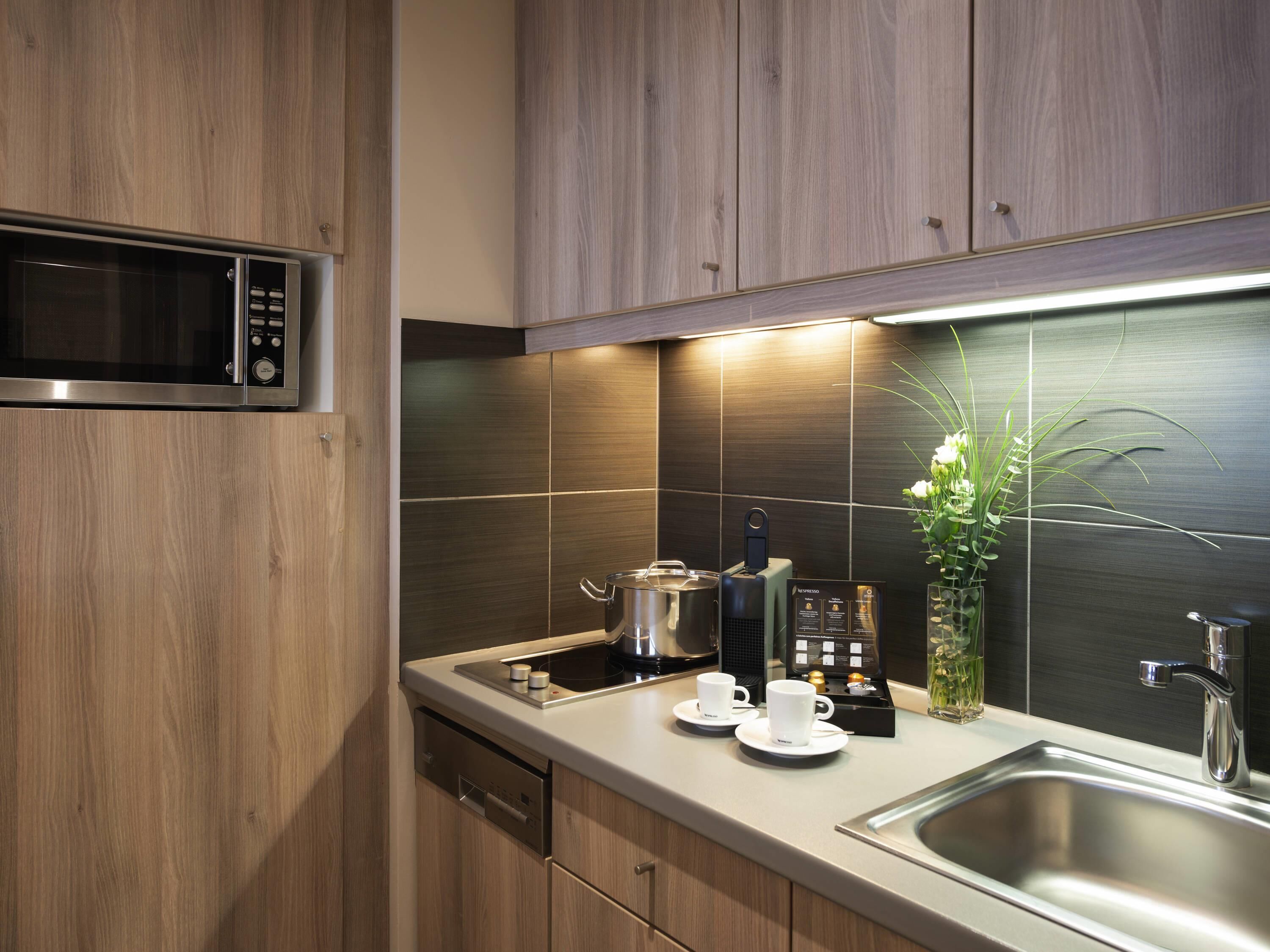 Una cocina moderna con armarios de madera, un lavamanos de acero inoxidable, un microondas y una cafetera.