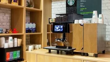Un mostrador de cafetería con una máquina de café Starbucks, un tablero de menú y varios productos de café en estantes.