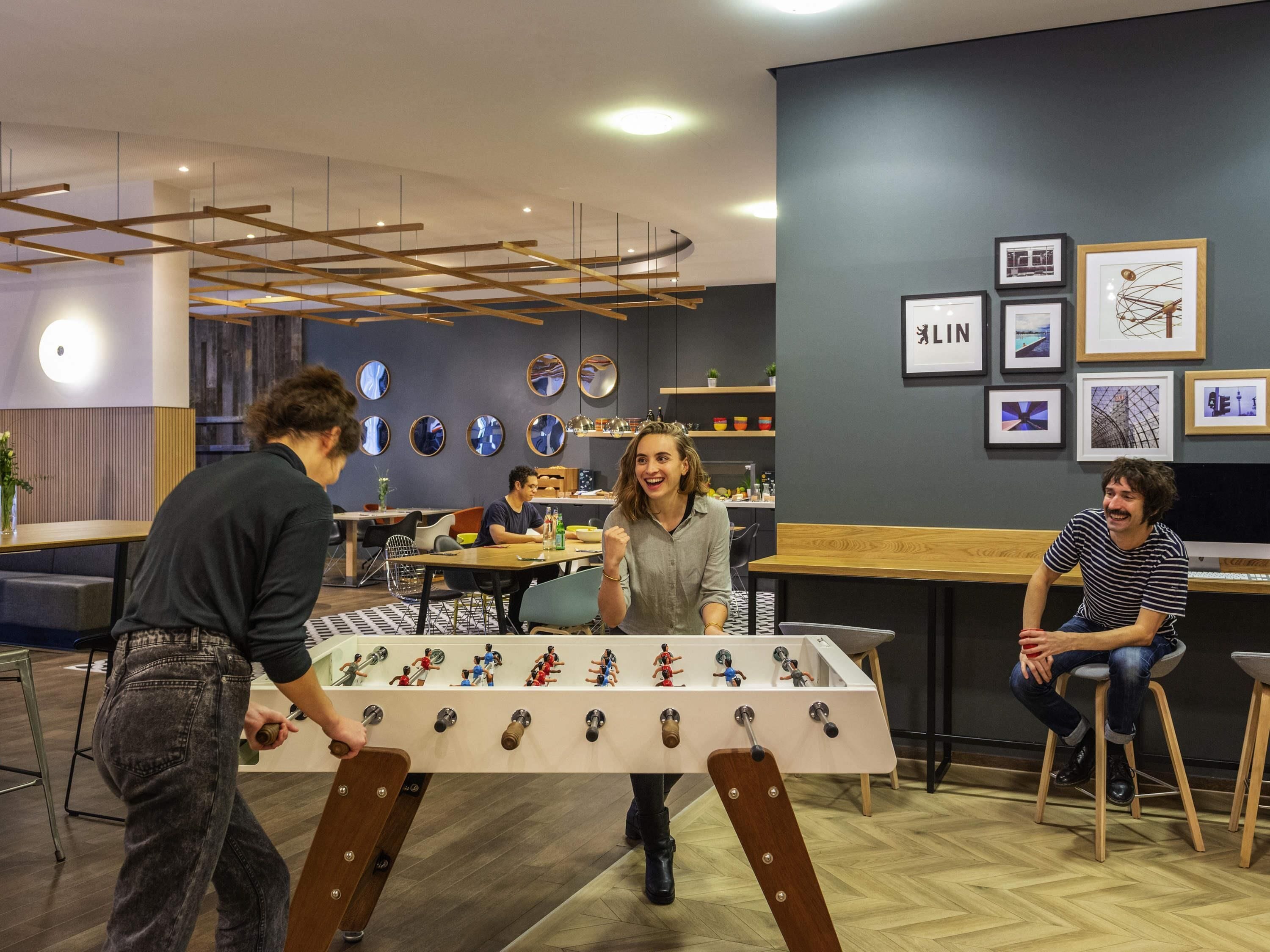 A modern indoor setting with a foosball table, seating areas, and artwork on the walls.