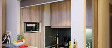 Una cocina moderna con armarios de madera, microondas integrado y una encimera con un cuenco de fruta y una botella de aceite de oliva.