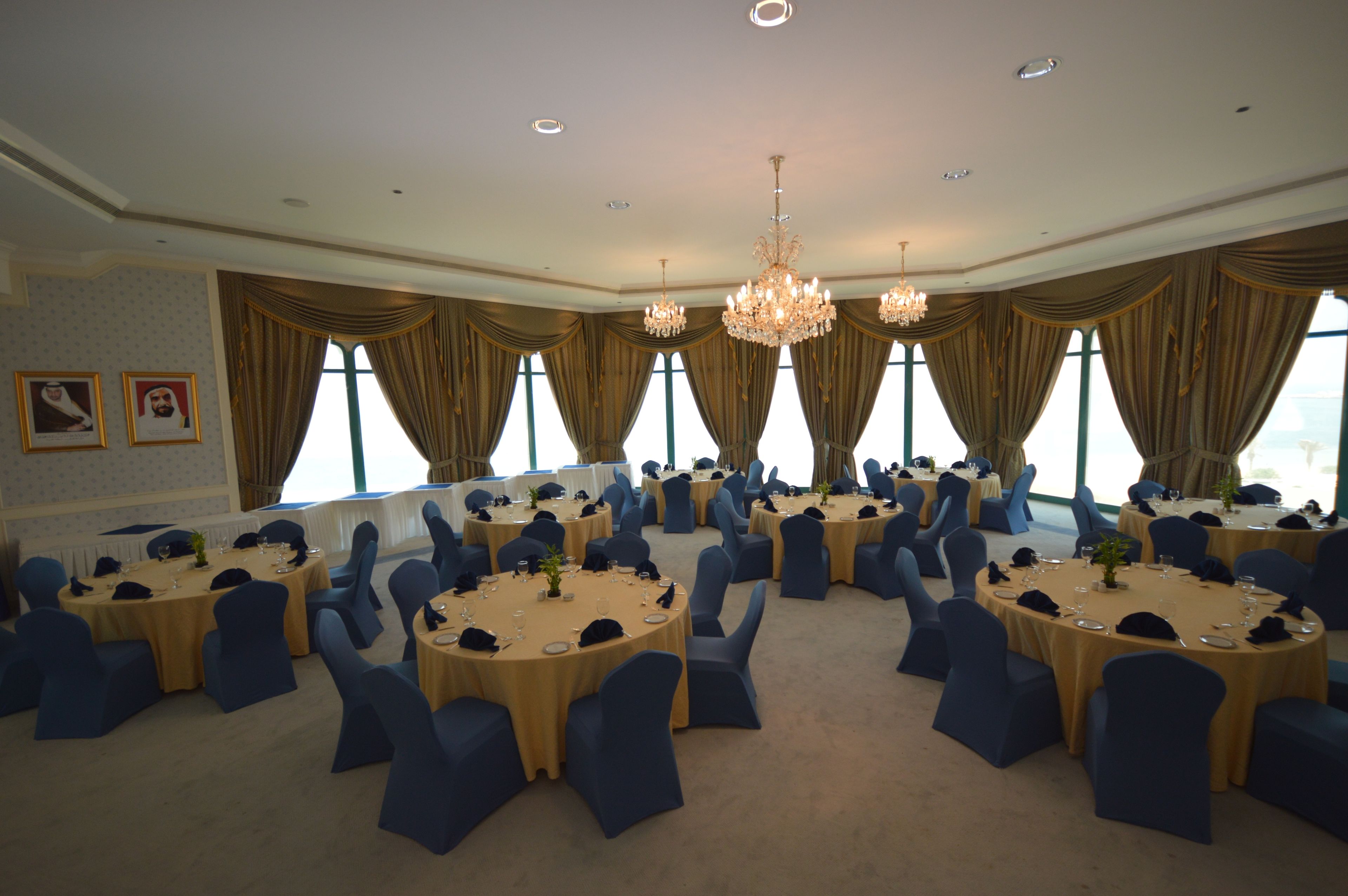 A large conference room with round tables, blue chairs, and chandeliers.