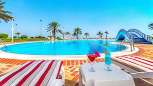 Un área de piscina con sillones de descanso, una mesa con bebidas y una vista despejada a la piscina.