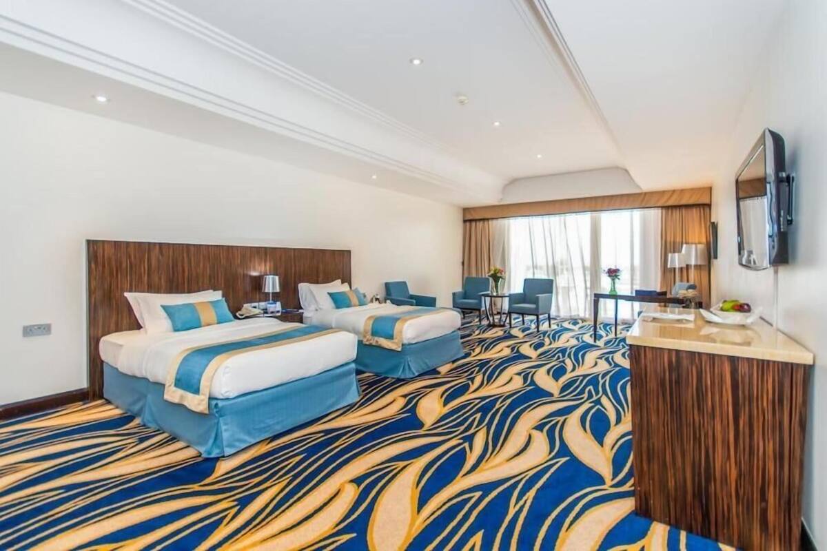 Habitación de hotel con dos camas, un escritorio, una silla y un ventanal grande.