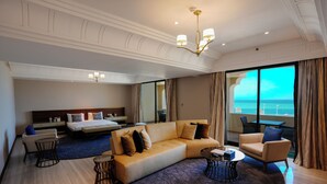 Habitación de hotel moderna con una cama grande, un sofá, una mesa de comedor y vistas al mar.
