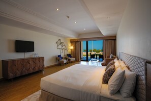 A modern hotel room with a large bed, a flat-screen TV, a wooden cabinet, and a balcony with a view. - Al Marfa Hotel (Al Mirfa)