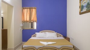 A bedroom with a bed, a window with curtains, a painting on the wall, and a bedside table. - Hotel Suriya International (Chennai)