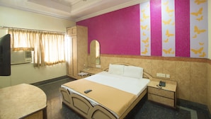 A hotel room with a bed, bedside table, nightstand, and a ceiling fan. - Hotel Suriya International (Chennai)