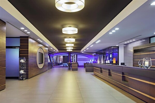 A modern hotel lobby with a reception desk, seating area, and a large screen.