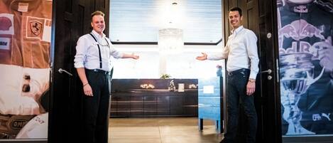 Dos hombres de pie en un vestíbulo con puertas abiertas, una araña de cristal y una recepción.