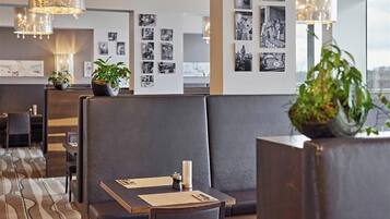 Eine moderne Hotellobby mit Ledersitzgelegenheiten, einem gemusterten Teppich und an Wänden befestigten Schwarzweißfotos.