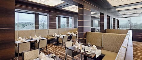 Un restaurante moderno con techos altos, ventanas amplias y una variedad de opciones de asientos, incluyendo mesas y cabinas.