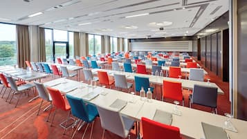 Un salón de conferencias con varias mesas y sillas, ventanas amplias y vistas al exterior.