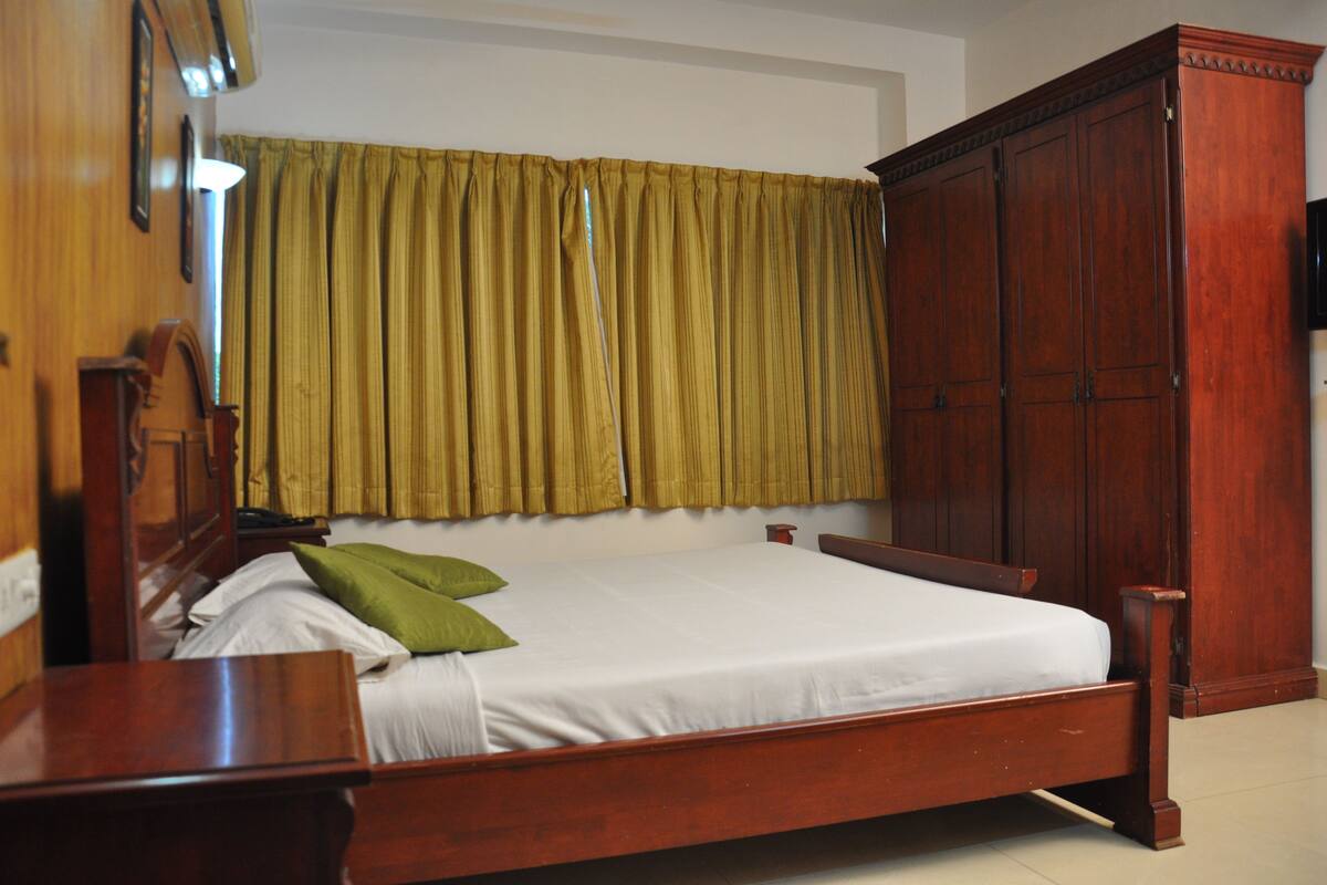Een houten bed met een witte matras en groene kussens, een houten nachtkastje en een grote houten garderobe.