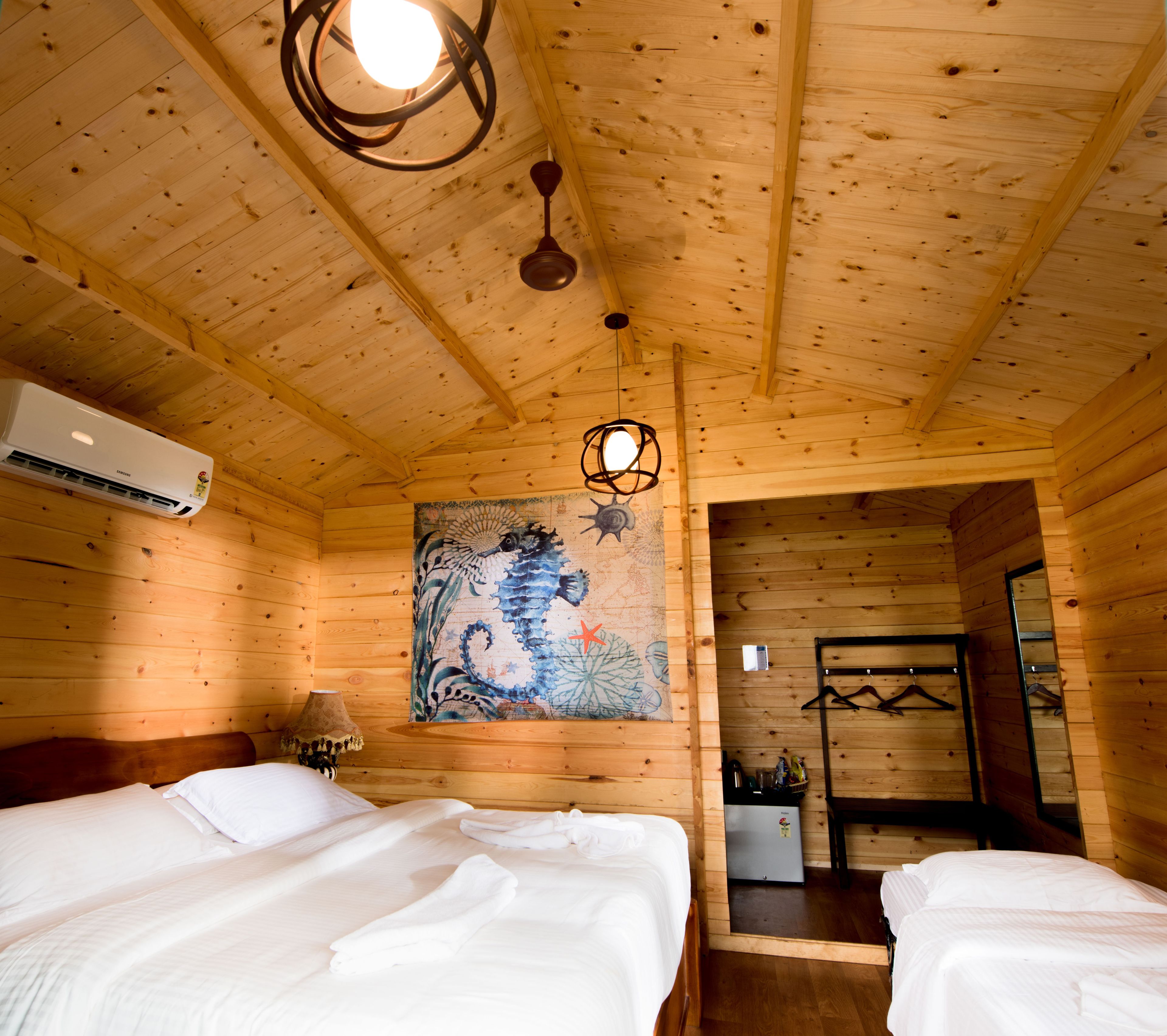 Habitación tipo cabaña de madera con dos camas, un ventilador de techo, un equipo de aire acondicionado y un cuadro en la pared.