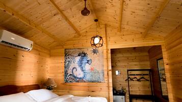 Habitación tipo cabaña de madera con dos camas, un ventilador de techo, un equipo de aire acondicionado y un cuadro en la pared.