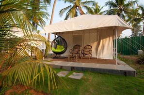 A covered outdoor seating area with a hanging chair and wicker chairs, surrounded by palm trees.