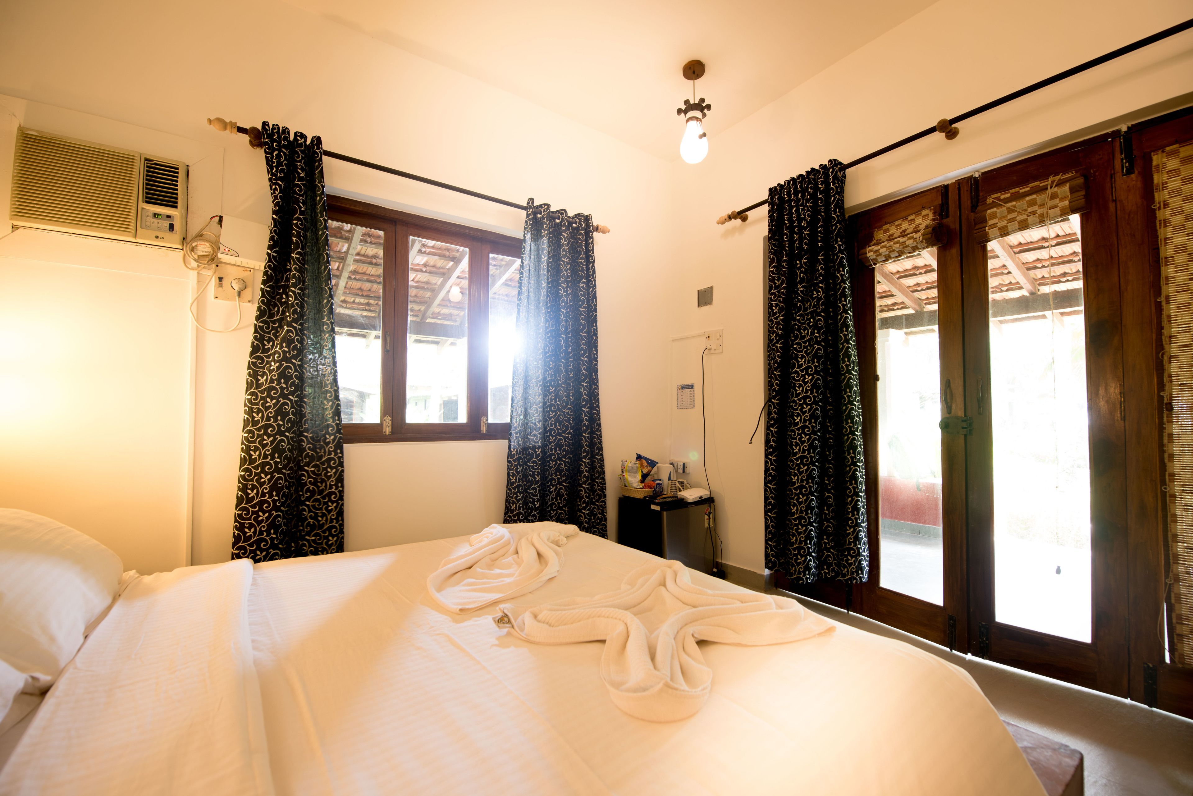 Una habitación de hotel con cama, ventana con cortinas, equipo de aire acondicionado y una lámpara en el techo.